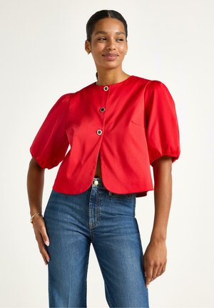 Rød cropped jakke med puffede ærmer, udstyret med rund halsudskæring og tre sorte knaplukninger. Båret over blå denim jeans.