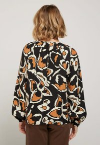 Blouse noire avec un motif abstrait orange et crème, à manches longues et col froncé. Tissu texturé avec une coupe ample.