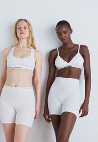 Bras e pantaloni sportivi bianchi di Calvin Klein con cintura elastica, tessuto liscio e design minimalista con accenti del logo.