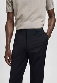Camisa beige de manga corta combinada con pantalones negros ajustados. Los pantalones tienen una textura suave y un corte recto, diseñados para un ajuste ceñido.