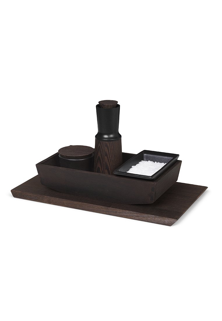 Ensemble de condiments en bois sombre sur un plateau rectangulaire, comprenant un moulin à poivre haut, un petit contenant rond et un plat carré avec du sel.