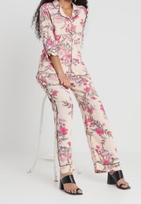 Set di pigiama floreale in tessuto morbido e leggero; presenta motivi di fiori rosa e blu su uno sfondo crema chiaro, con piping nero a contrasto.