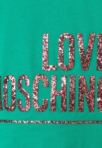Grön tyg med stora glittriga röda och silverbokstäver som stavar "LOVE MOSCHINO" och en glittrig understrykning under texten.