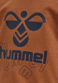 Brązowa bawełniana koszula z dużą granatową grafiką z stylizowanym wzorem pszczoły oraz widocznie wyeksponowaną nazwą marki "hummel".