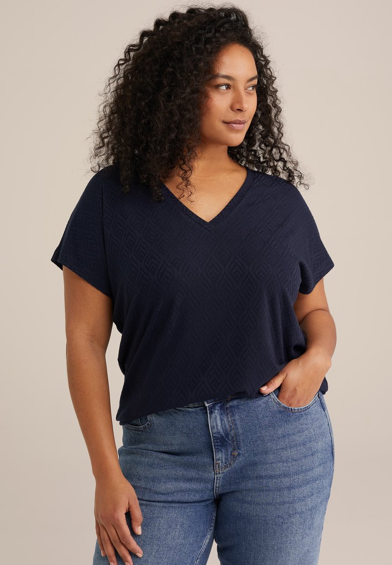 Mörkblå V-ringad skjorta med korta ärmar, prydd med ett texturerat geometriskt mönster, kombinerad med blå denimjeans.