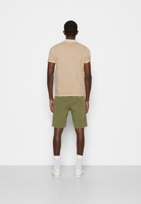 Beige pikétröja med korta ärmar, olivgröna shorts, vita strumpor och vita sneakers. Enkel design och normal passform.