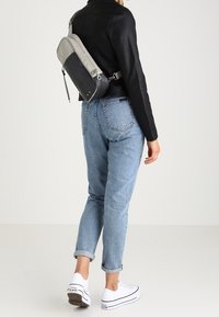 Szara i czarna torebka na ramię wykonana z materiału syntetycznego, o eleganckim wzornictwie, gładkiej fakturze i regulowanym pasku, noszona na plecach modelki.