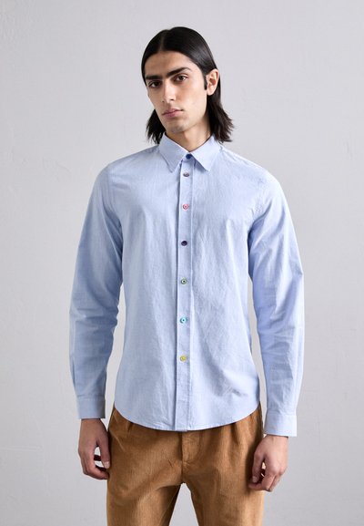 Chemise bleu clair à manches longues avec un col pointu et des boutons colorés. Dotée d'une texture en coton lisse, accompagnée de pantalons en velours côtelé beige.