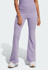 Rozšírené športové nohavice svetlofialovej farby s hladkou textúrou, na ľavom stehne majú malé logo a sú doplnené bielymi teniskami.