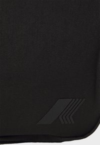 Sac à dos en tissu noir avec une texture lisse, présentant un logo embossé élégant dans le coin inférieur. Design minimaliste sans détails supplémentaires.