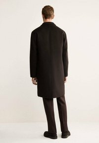Cappotto lungo nero in lana, caratterizzato da un taglio dritto e design minimalista, mostrato da dietro con una consistenza liscia e senza motivi.