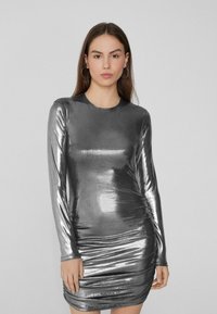 Metaliczna srebrna sukienka z długim rękawem o dopasowanym kroju, z marszczonymi bokami dla nadania faktury oraz okrągłym dekoltem. Gładki, błyszczący materiał.
