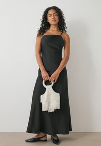 Melnas satīna kleitas ar taisnu kakla izgriezumu un plānām siksnām, kopā ar baltu frinšu rokassomu un melniem dzīvokļiem. Gluda tekstūra un tīras līnijas.