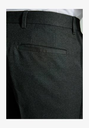 Pantalones de tela negra texturizada con una cinturilla suave, que cuentan con un único bolsillo trasero con un ribete de tela a juego.
