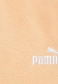 Ferskenfarvet stof med en blød tekstur, der har et hvidt broderet "PUMA" logo og et stilig Puma ikon.