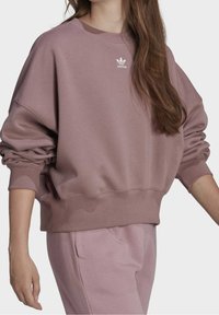 Överdimensionerad mauve sweatshirt med elastiska mudd och nederkant, prydd med en liten vit Adidas-logga på bröstet och en mjuk, texturerad tyg.