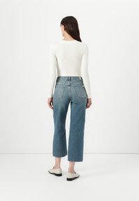 Tett hvit ribbestrikket langermet topp kombinert med høyt midje lette blå straight-leg denimjeans. Uformelle sko med lav hæl.