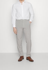 Camisa blanca abotonada combinada con pantalones ajustados grises claros y zapatos de cuero marrón. Textura suave y diseño entallado.