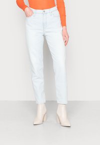 Jeans de cintura alta de color azul claro con pierna recta, confeccionados en denim. Llevados con una blusa de manga larga naranja y botas de tobillo de tacón grueso beige.