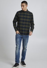 Rutete skjorte med knapp i mørkeblå og olivengrønn, lange ermer, laget av bomull. Kombinert med lyseblå jeans og svarte joggesko.