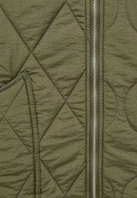 Tissu matelassé vert avec couture en losange, doté d'une fermeture éclair en métal et d'une couture de poche sur le côté gauche.