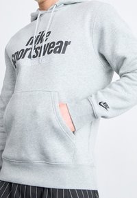 Gray fleece hoodie with a front pocket, featuring a black printed logo and text. Includes drawstrings and ribbed cuffs.