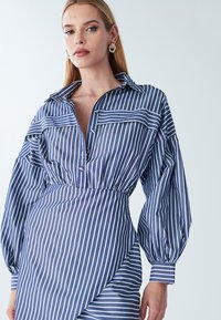 Pruhované šaty v námořnické modré a bílé barvě, s límečkem, knoflíkovou légou, dlouhými puff rukávy a asymetrickým lemem. Hladká látka.