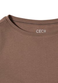 Camiseta de algodón marrón con cuello redondo, textura sutil y una pequeña etiqueta "CECII" en gris claro en la parte posterior del cuello.
