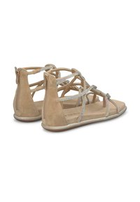 Beige suède sandalen met kruiselings banden en zilveren accenten. Achterste ritssluiting; platte zool met metallic rand. Zacht, textuurmateriaal.