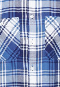 Modrá a bílá kostkovaná košile s button-up designem, dvěma kapsami na hrudi a texturovanou bavlněnou tkaninou v různých odstínech modré.