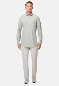 Camisa de manga larga gris claro con botones al frente, textura suave y dobladillo redondeado, combinada con pantalones de color claro y zapatillas deportivas.