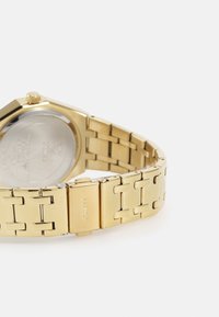 Gouden metalen polshorloge met een achthoekige kast, een schakelarmband en een klapsluiting. Heeft een gladde achterkant en minimale details.