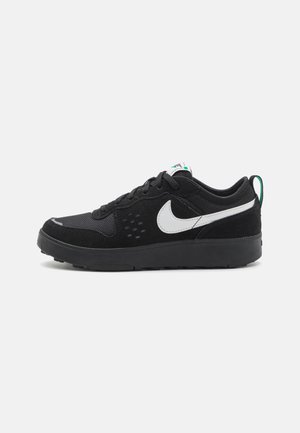 Czarny sneaker Nike z białym logo, sznurowany, z siateczkową i zamszową cholewką oraz zieloną pętelką na pięcie, widok z boku.