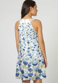 Vestido floral con base blanca decorada con flores azules, diseño sin mangas y cierre de cremallera en la parte posterior. Textura suave y corte relajado.