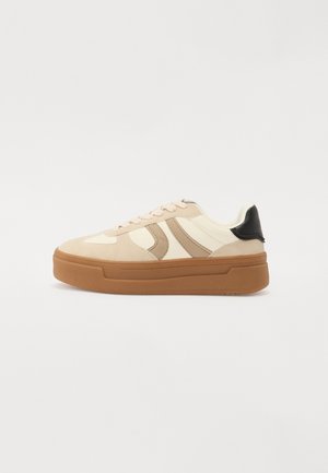 Roomkleurige en beige lage sneaker met bruine dikke zool en zwarte hieltab, zijkanten met strepen en vetersluiting.
