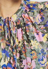 Blouse florale avec un mélange de teintes rose, jaune et verte. Décolleté en V avec un détail à nouer, design à épaule plissée et tissu léger.