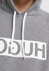 Felpa grigia con un logo bianco sul petto, dotata di lacci bianchi e un tessuto morbido e testurizzato.