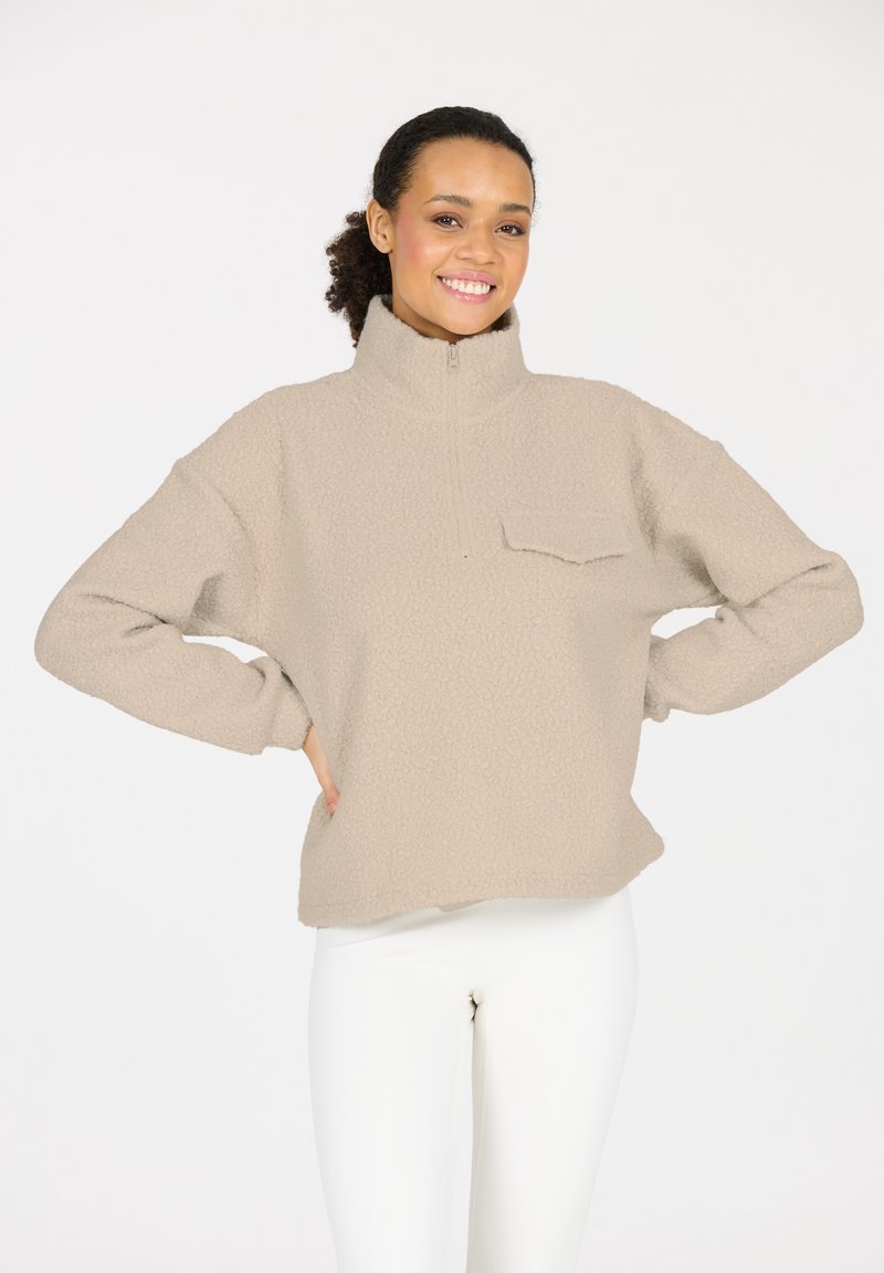 Beiger Fleece-Pullover mit hohem Kragen, Viertelreißverschluss und einer aufgesetzten Tasche. Mit strukturiertem Material und lockerer Passform.