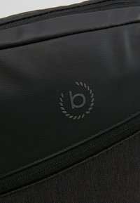 Borsa in tessuto nero con texture, dotata di una parte superiore liscia, caratterizzata da un logo grigio all'interno di un motivo circolare a foglia. Apertura con zipper nella parte superiore.