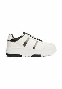 Witte sneaker met een gestructureerd leren bovenwerk, zwarte accenten en twee metalen strepen. Dikke witte zool met een zwarte rubberen onderkant. Standaard veters.