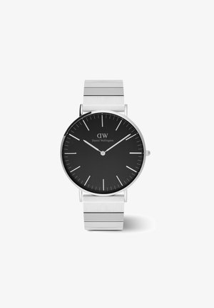 Reloj de esfera negra con correa de acero inoxidable plateado. Presenta un diseño minimalista, marcadores de hora delgados y el logo de la marca ubicado debajo de la posición de las 12 en punto.