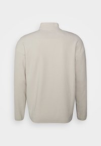 Lys beige langærmet fleecepullover med høj krave, vist fra ryggen mod en ensfarvet hvid baggrund.