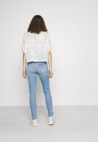 Top recortado con estampado de flores en colores pastel; vaqueros ajustados de color azul claro; zapatillas de color claro; cabello rizado visible.