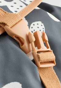 Gray fabric with white polka dots features a light brown buckle and strap. Close-up shows texture and design details.