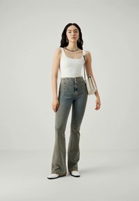 Bijela majica bez rukava, traperice s visokim strukom u svijetloplavoj boji, širi kroj, svijetli ton, prednji gumbasti kopčanje, model drži malu torbicu.