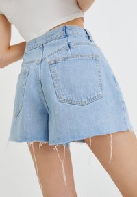 Shorts de mezclilla azul claro con dobladillo deshilachado, diseño de cintura alta, costuras gruesas y dos bolsillos traseros visibles.