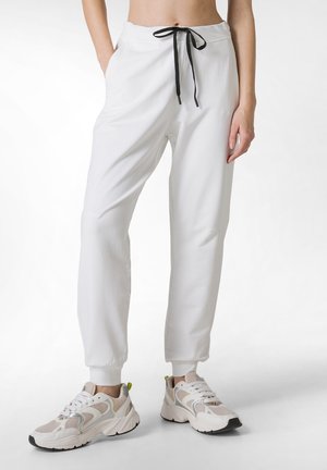Witte joggerbroeken met elastische boorden, een trekkoord in de taille, twee zijzakken, gecombineerd met beige en witte sportschoenen met zwarte zolen.