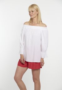 Weißes, schulterfreies Blusenshirt mit langen Ärmeln, elastischem Ausschnitt und gerafften Manschetten; kombiniert mit roten Shorts aus leichtem Stoff, lässiges Design.