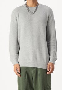 Maglione grigio chiaro con un motivo a maglia testurizzato, scollo rotondo, e polsini e orlo a costine. Abbinato a pantaloni cargo verdi.