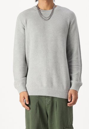 Maglione grigio chiaro con un motivo a maglia testurizzato, scollo rotondo, e polsini e orlo a costine. Abbinato a pantaloni cargo verdi.